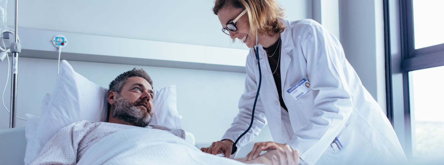Ein Patient im Krankenhausbett wird von einer Ärztin untersucht.