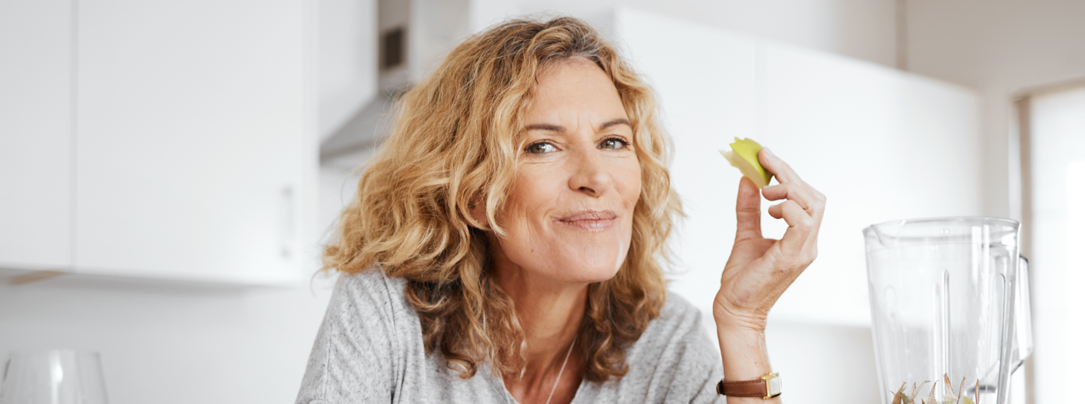 Eine Frau lächelt und hält ein angebissenes Obststück in der Hand.