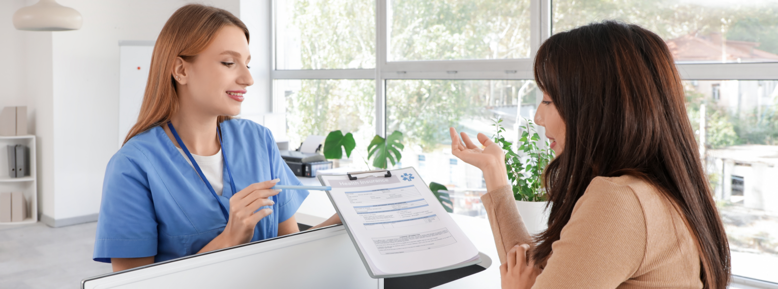 Eine medizinische Fachangestellte und eine Patientin besprechen am Empfang den Versicherungsstatus der Patientin.