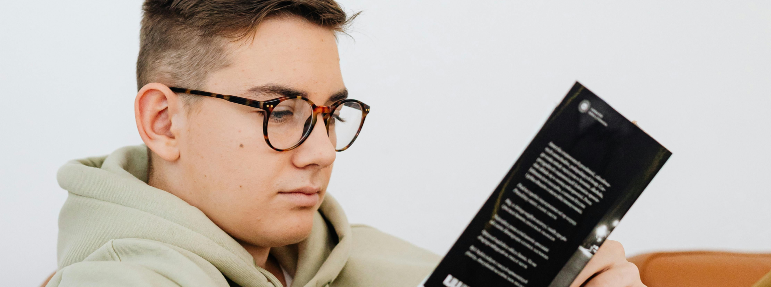 Ein Junge trägt eine Brille und liest ein Buch.