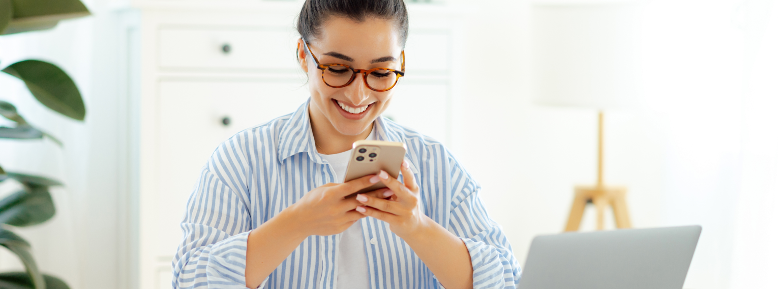 Eine lächelnde Frau schließt an ihrem Handy eine Krankenzusatzversicherung ab.