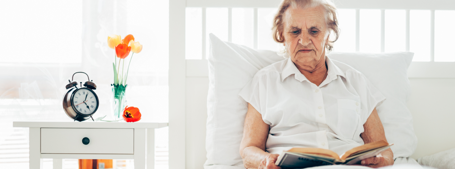 Eine ältere Frau liegt in einem Einzelzimmer im Krankenhaus und liest ein Buch.
