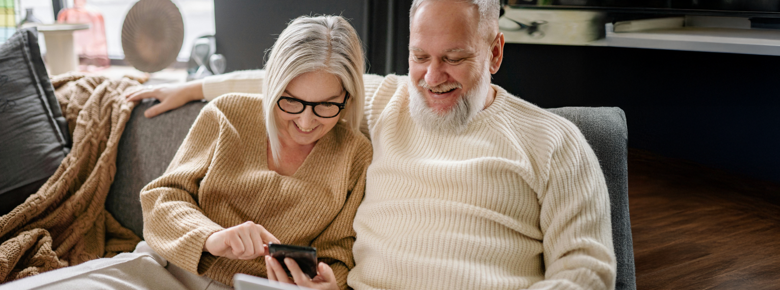Ein älteres Paar bestehend aus Frau und Mann schauen auf ihrem Handy nach einer Krankenzusatzversicherung für Rentnerinnen und Rentner.