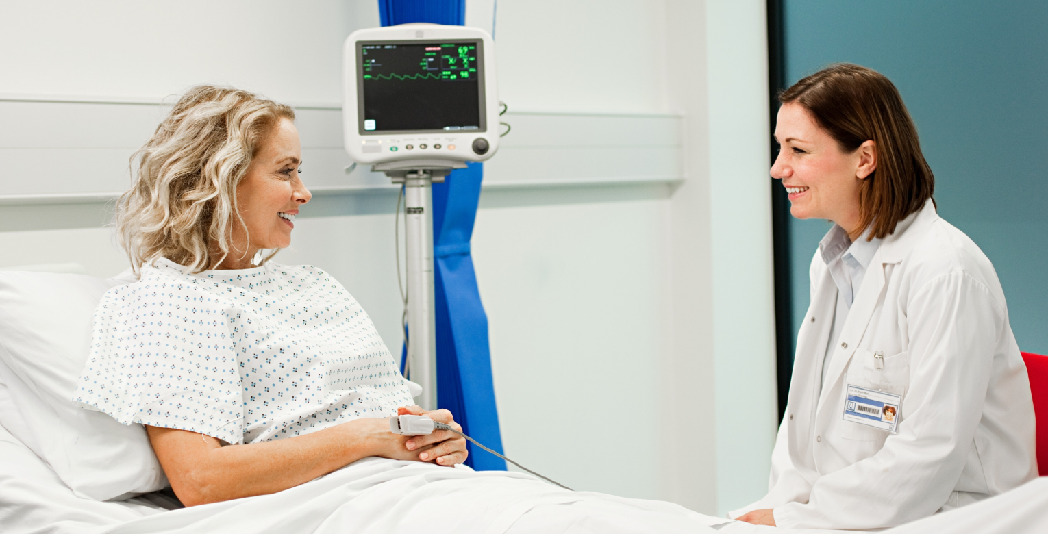 Eine Patientin im Krankenhausbett redet mit einer Ärztin.