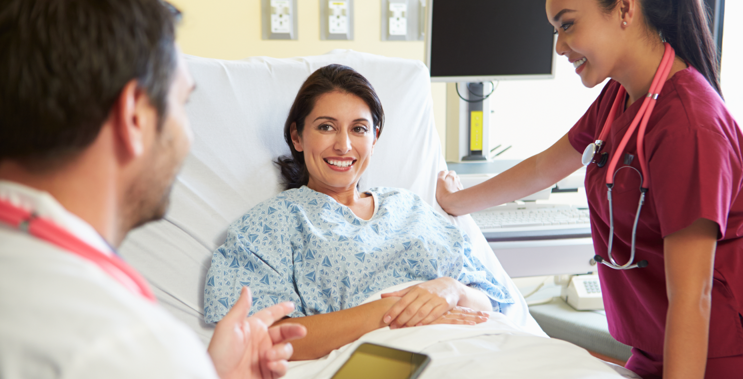 Eine Patientin mit Krankentagegeldversicherung liegt in einem Krankenhausbett und spricht mit einem Arzt und einer Krankenpflegerin.