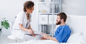 Ein Patient in einem Krankenhausbett spricht mit einer Ärztin.