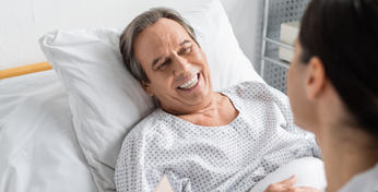 Eine Person mit Krankenhauszusatzversicherung liegt in einem Krankenhausbett und spricht mit einer Ärztin.